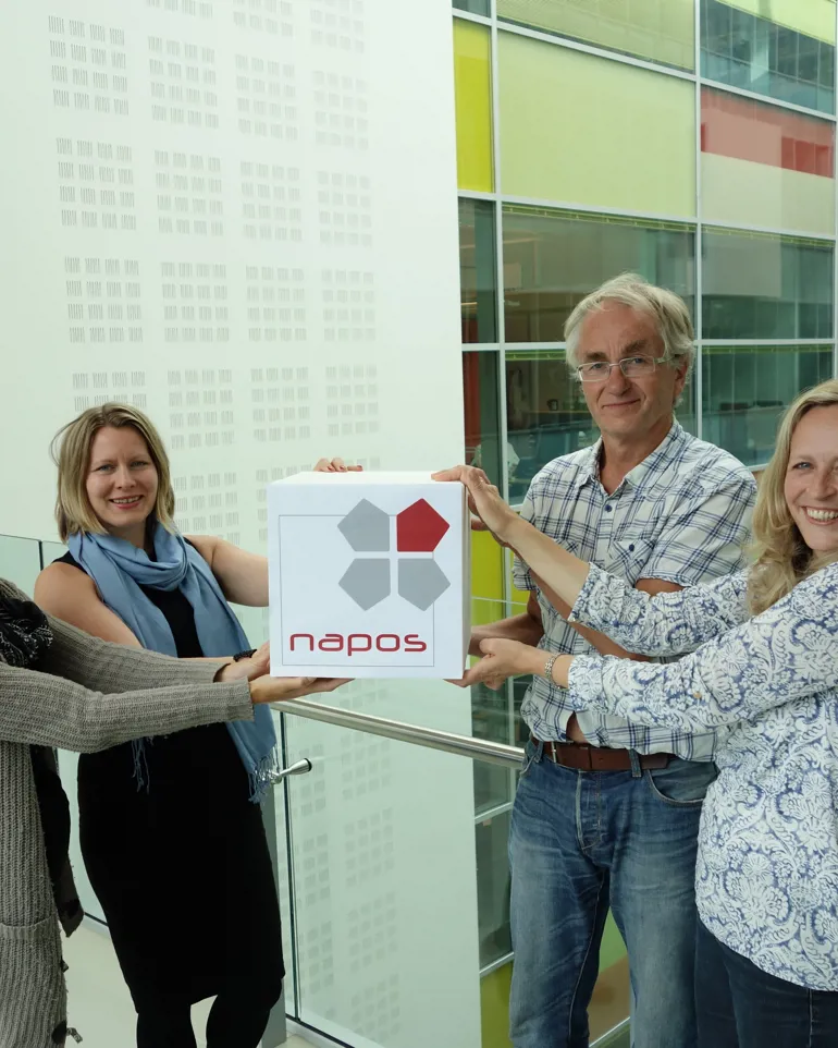 Fire ansatte ved NAPOS holder en boks med logo