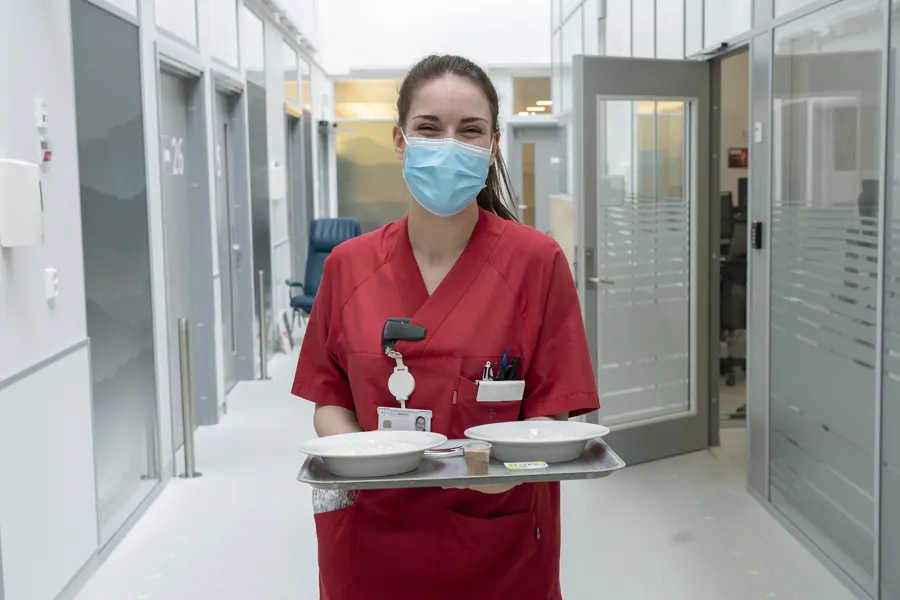 En person som har på seg maske og holder en tallerken med mat