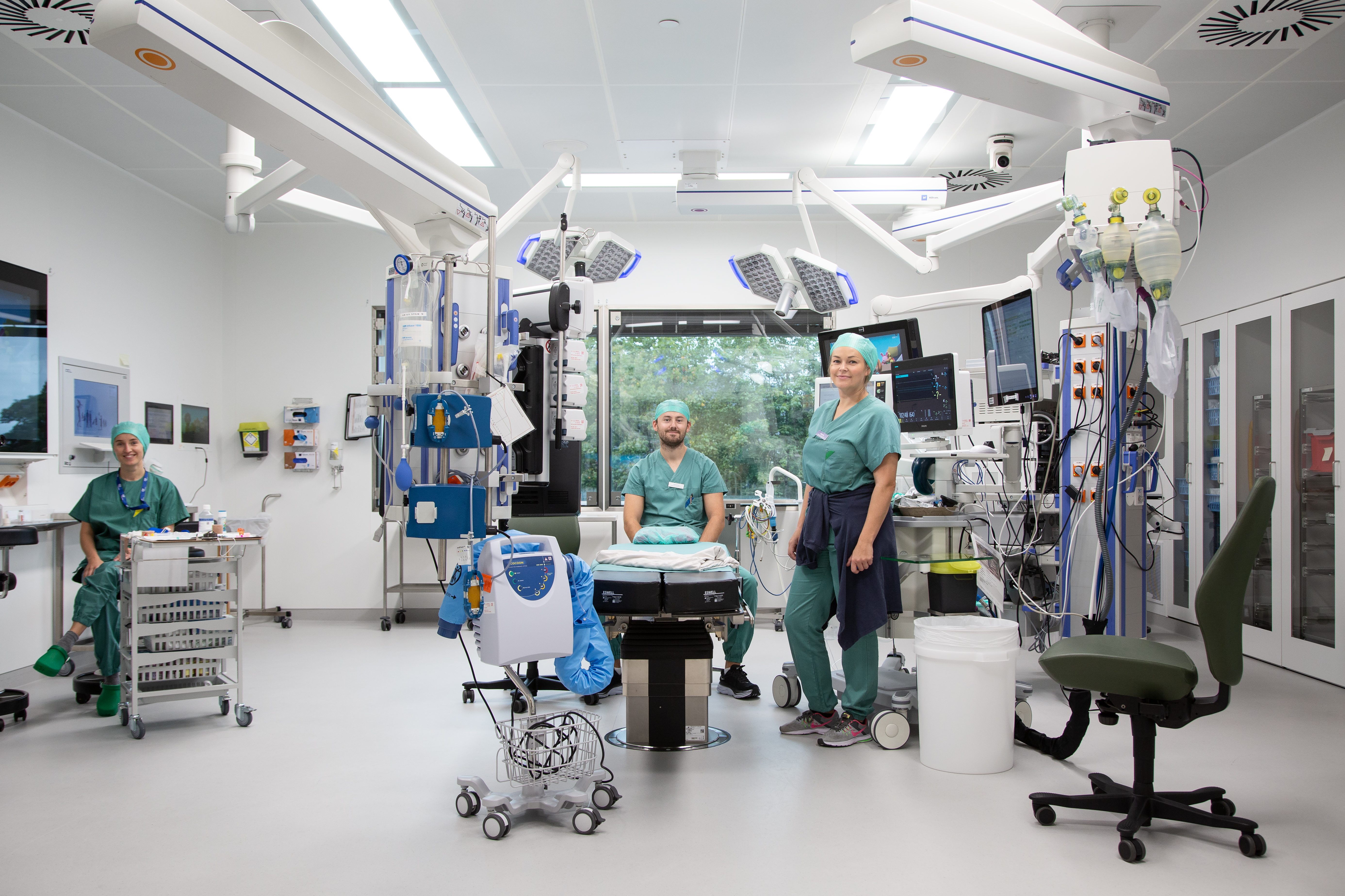 Tre personer i sykehusklær som står i en operasjonsstue