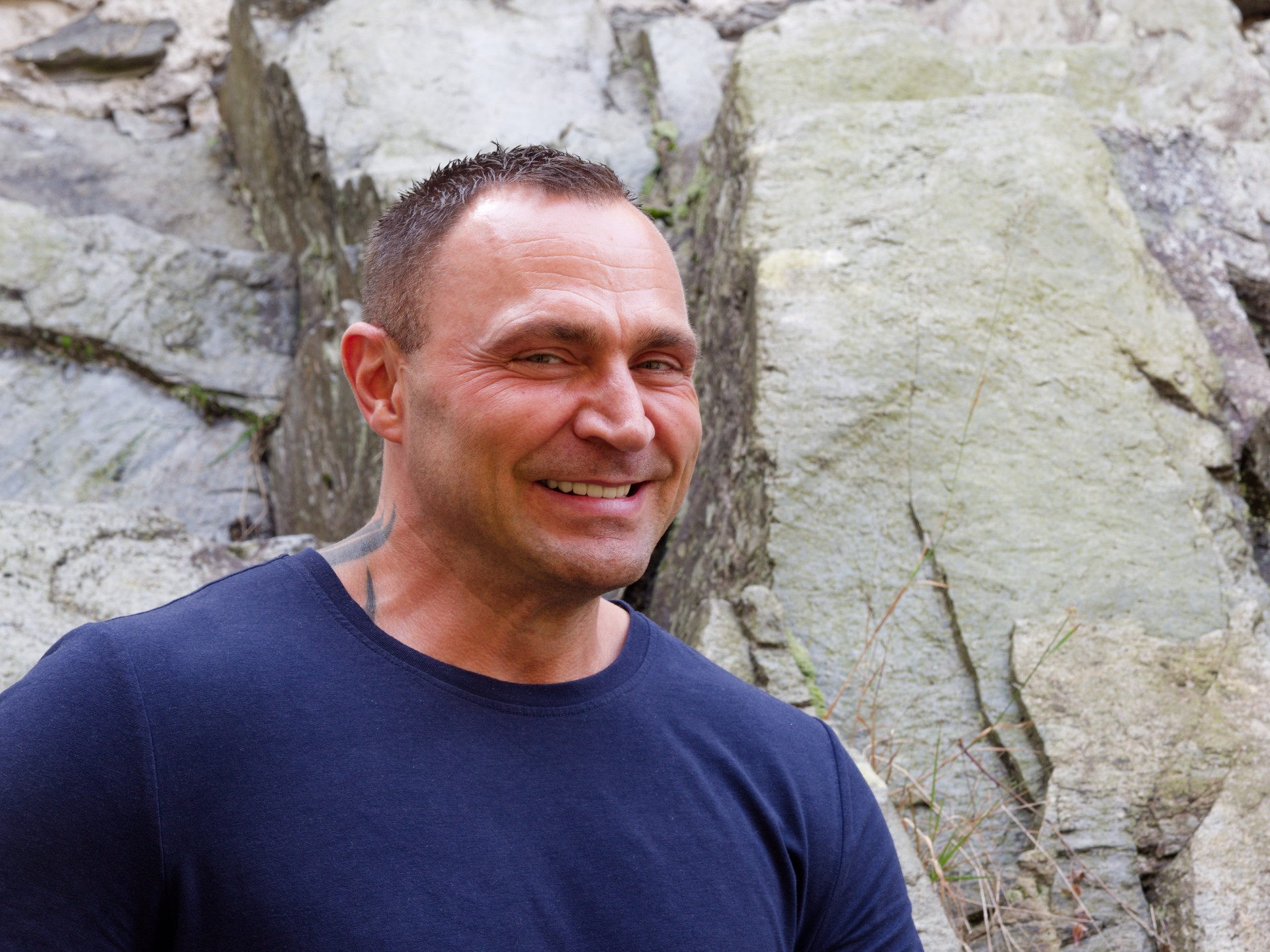 En mann som smiler foran en steinvegg