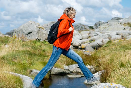 En person som har på seg en ryggsekk og går på steiner i fjellet.