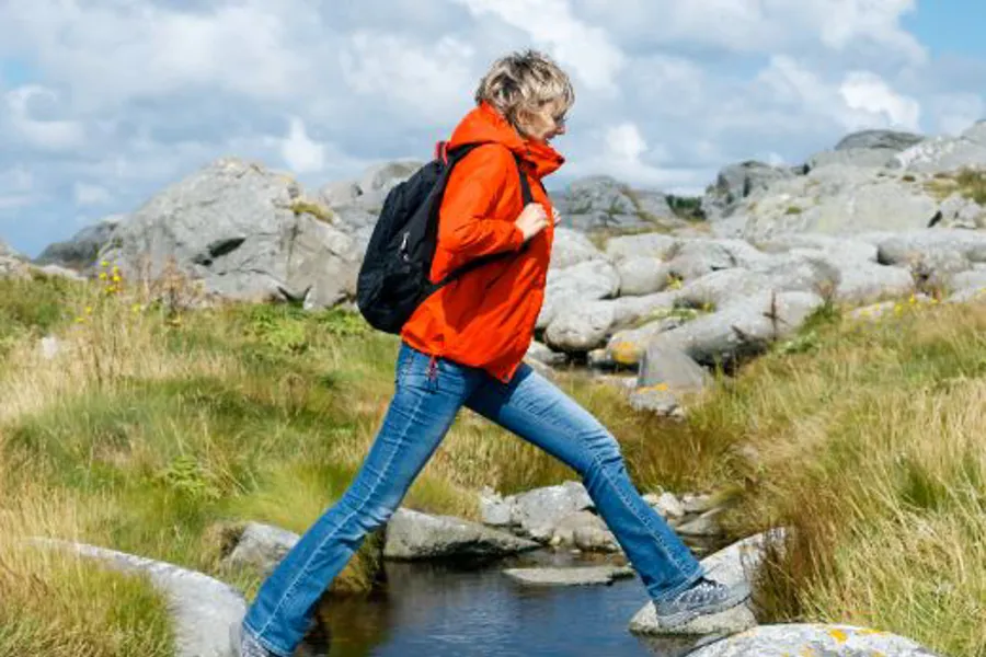 En person som har på seg en ryggsekk og går på steiner i fjellet.