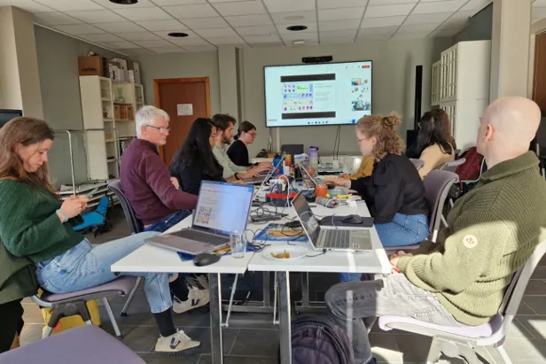 En gruppe mennesker som sitter rundt et bord med bærbare datamaskiner