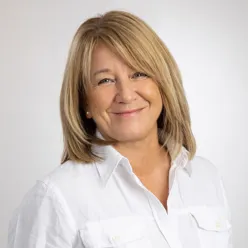 Portrett Maribeth Caya Rivelsrud. Kvinne som smiler i hvit skjorte.