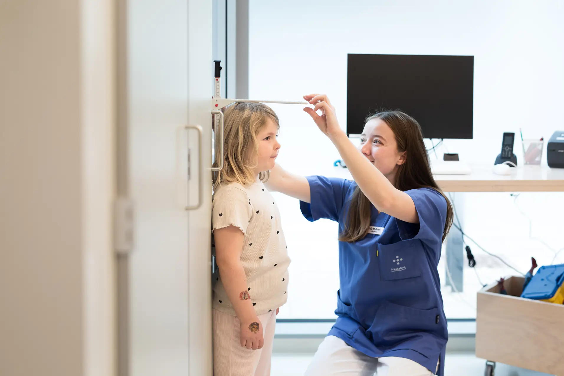 Et barn står inntil en vegg mens en voksen måler høyden