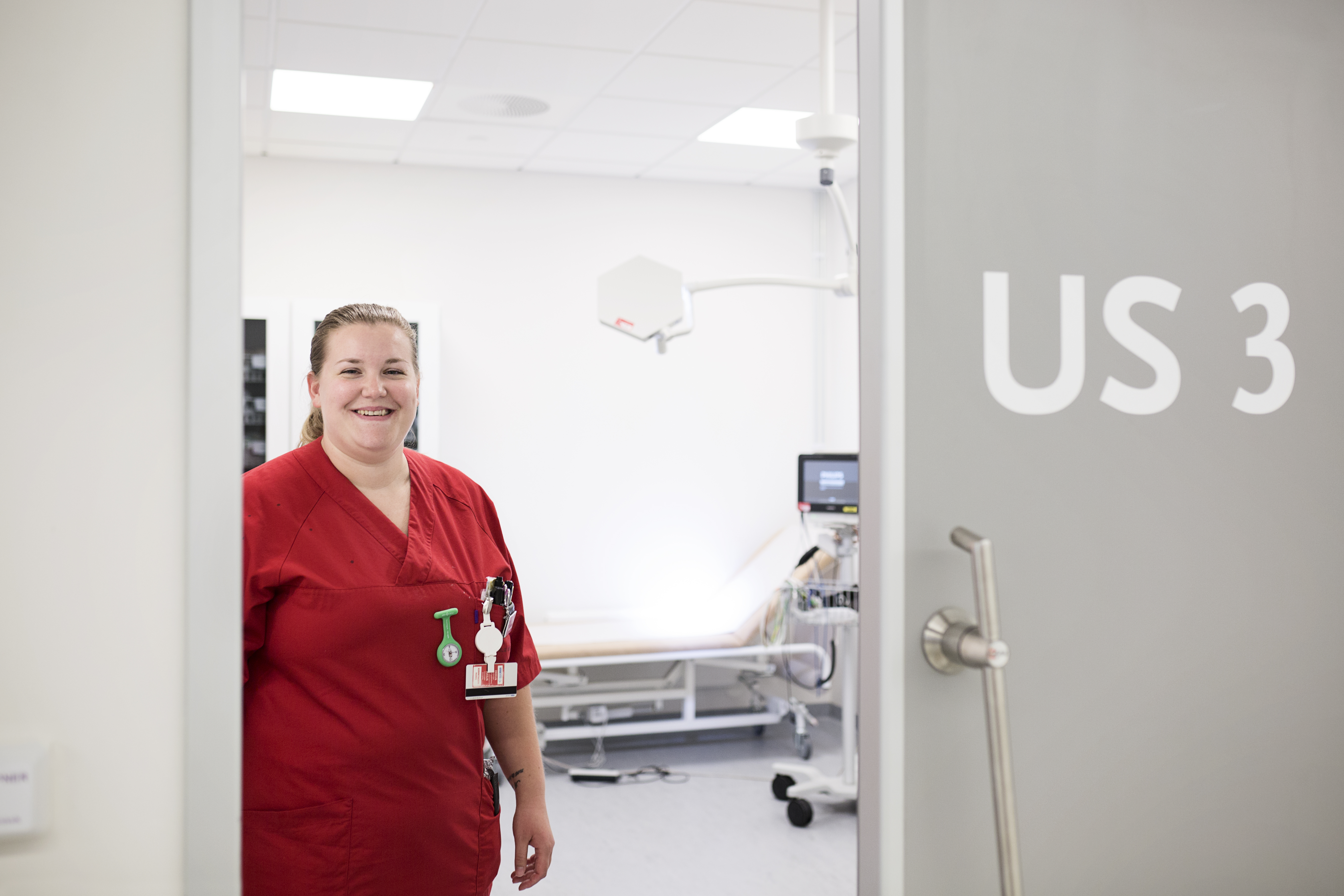 Helsefagarbeider i rød kittel står i døren inn til mottaksrom