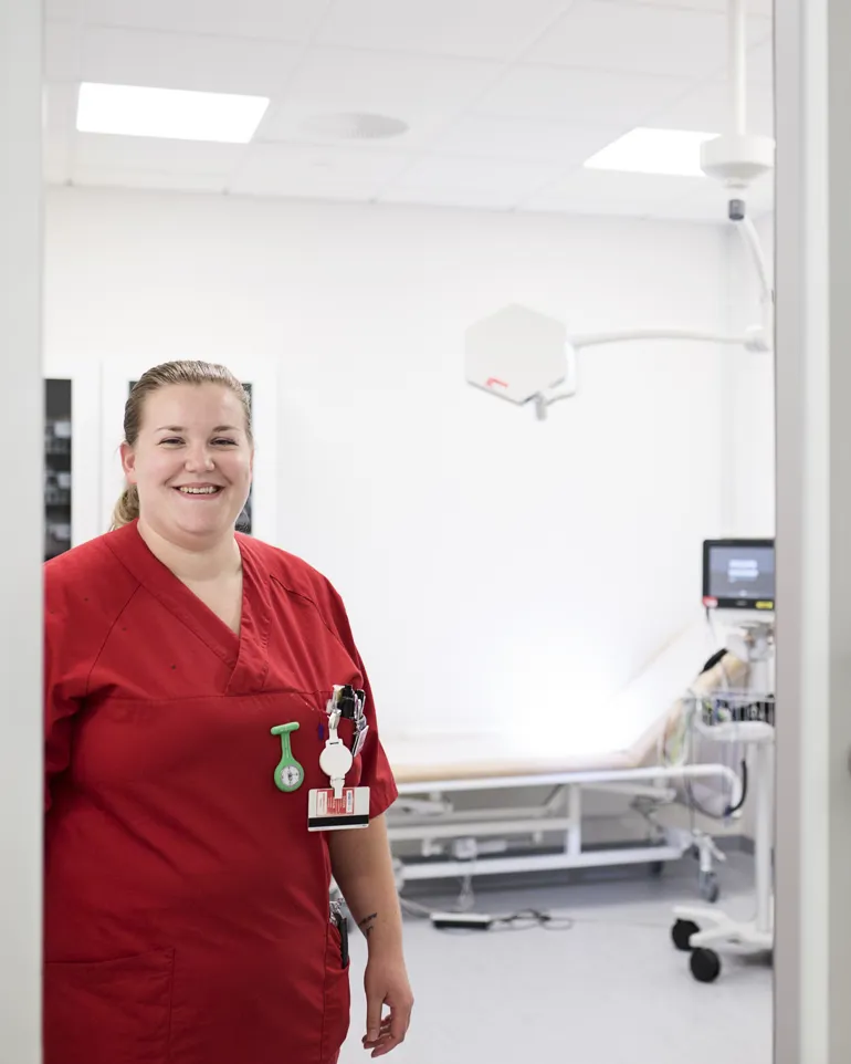 Helsefagarbeider i rød kittel står i døren inn til mottaksrom