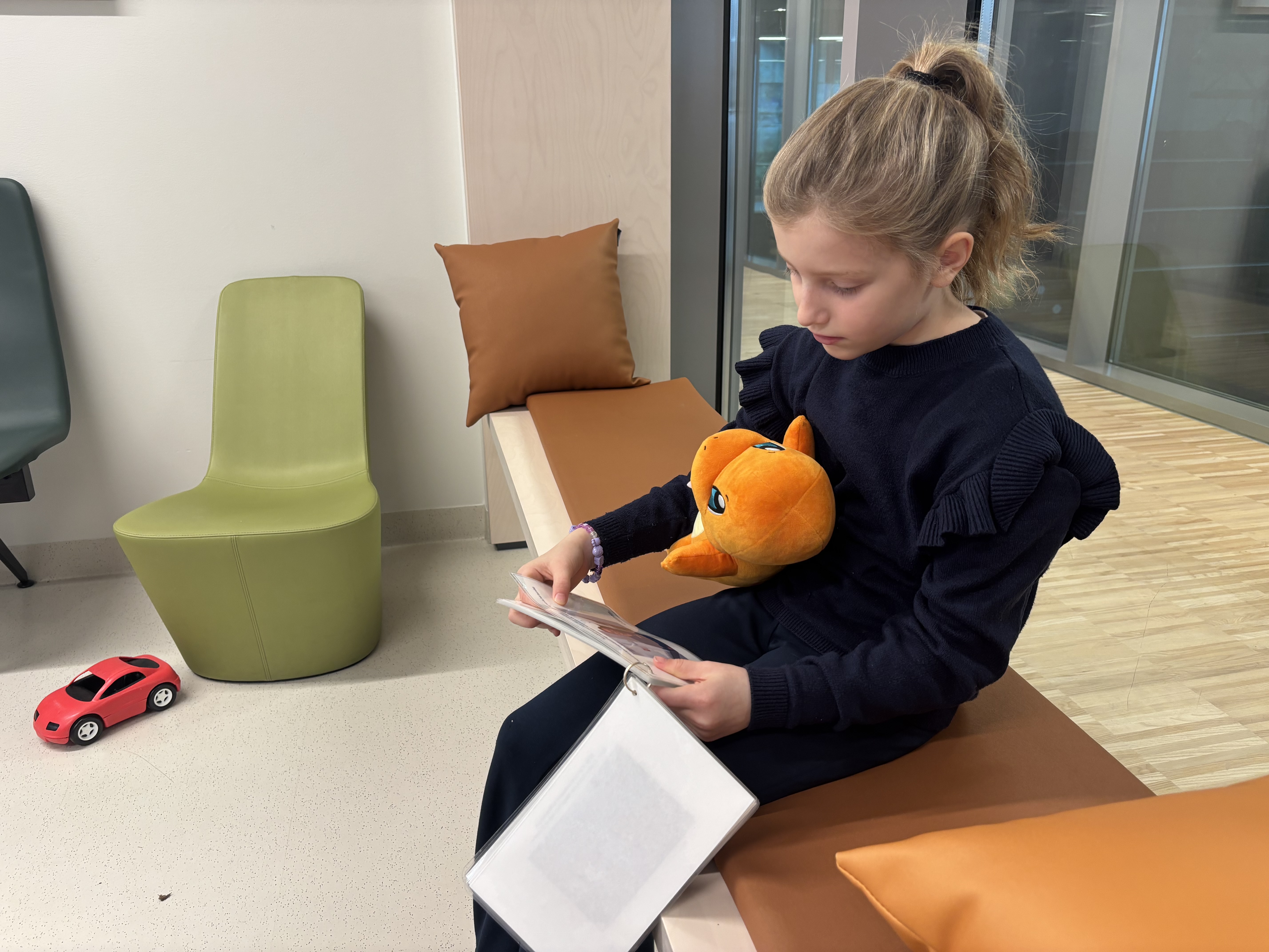 En jente som sitter å leser med et kosedyr i fanget