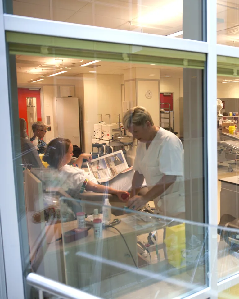 Utsikt fra gangbro inn i tappesal med helsepersonell og blodgivere som gir blod på Blodbanken Haukeland. Foto