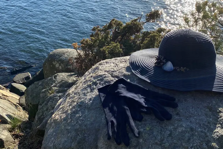 En hatt og hansker på en stein ved vann