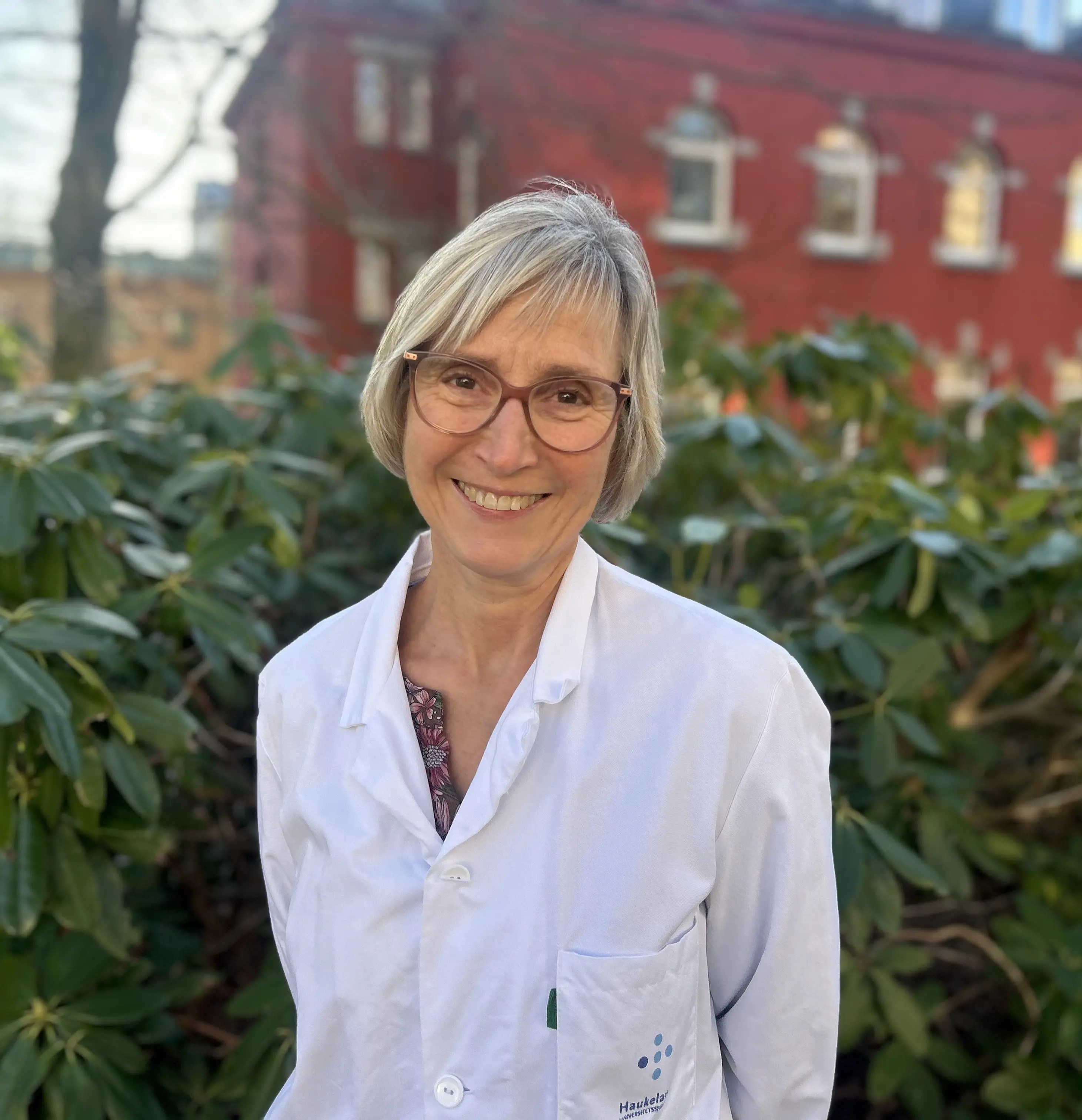 En person som smiler foran et rødt hus