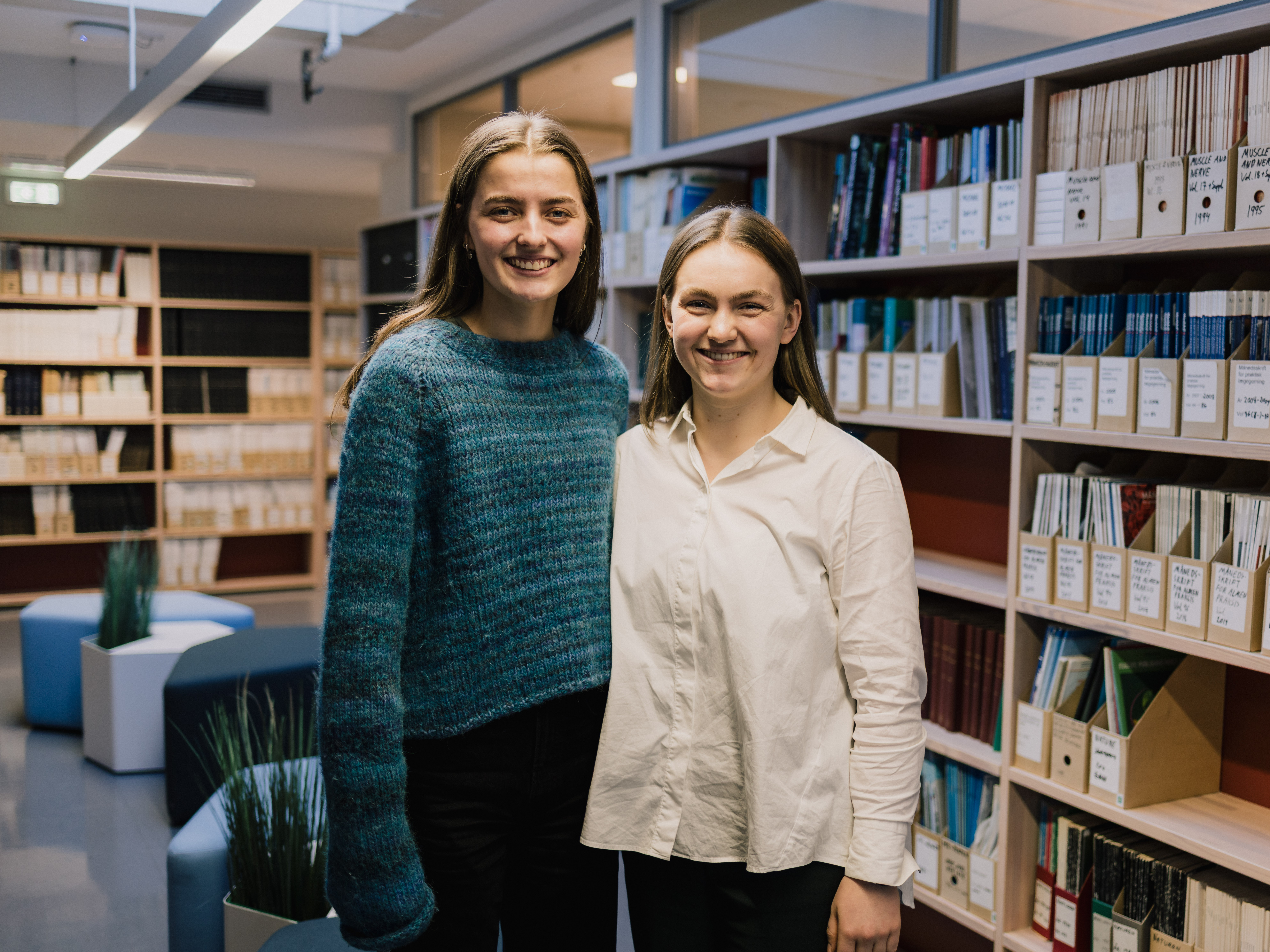 Et par kvinner som står foran en bokhylle