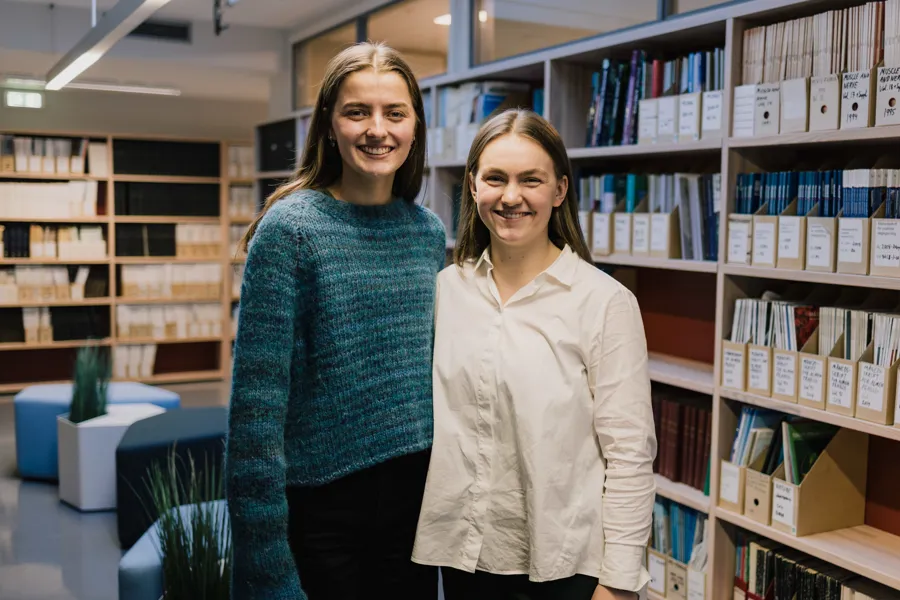 Et par kvinner som står foran en bokhylle