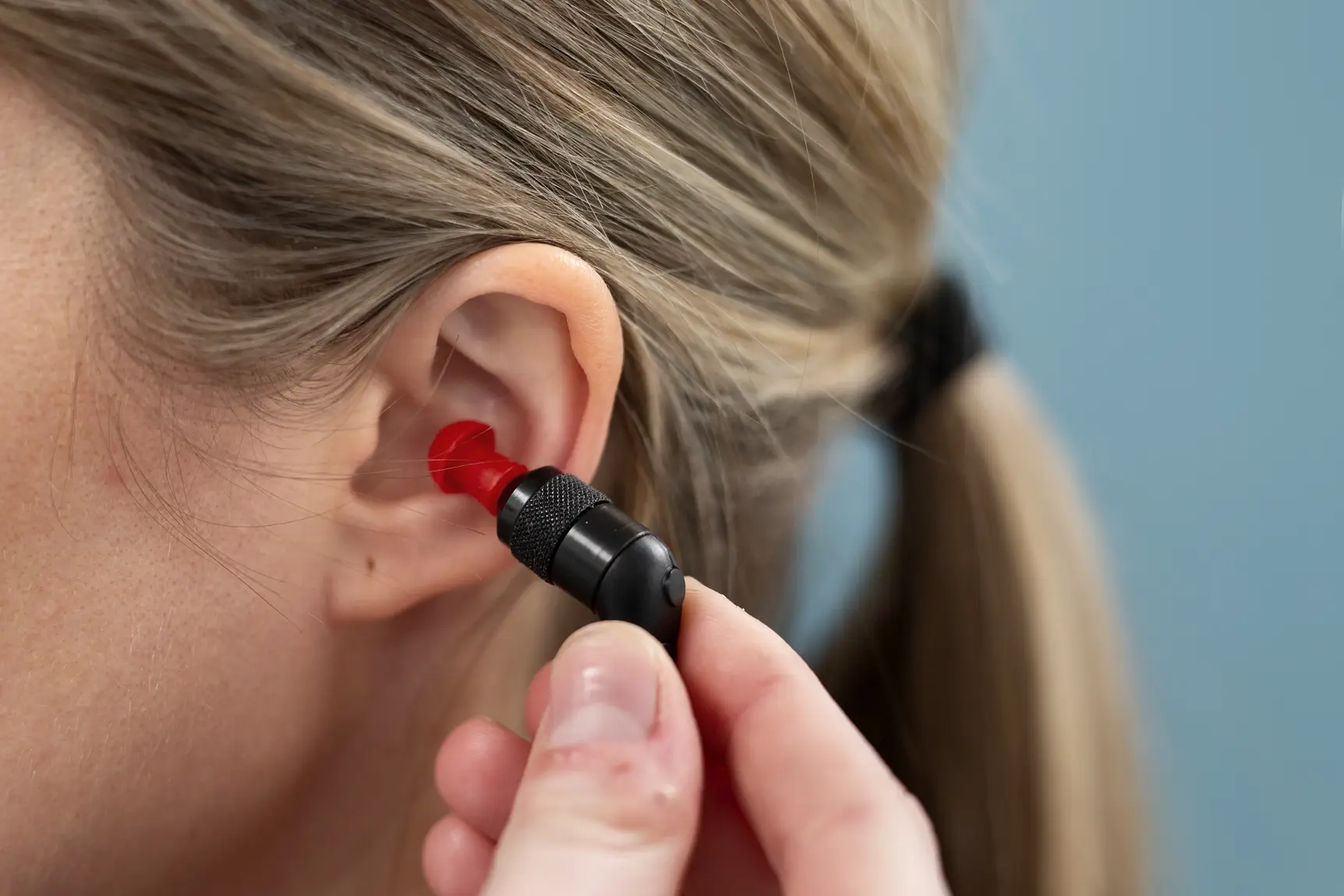En hånd som plasserer en propp inn i øret til en jente
