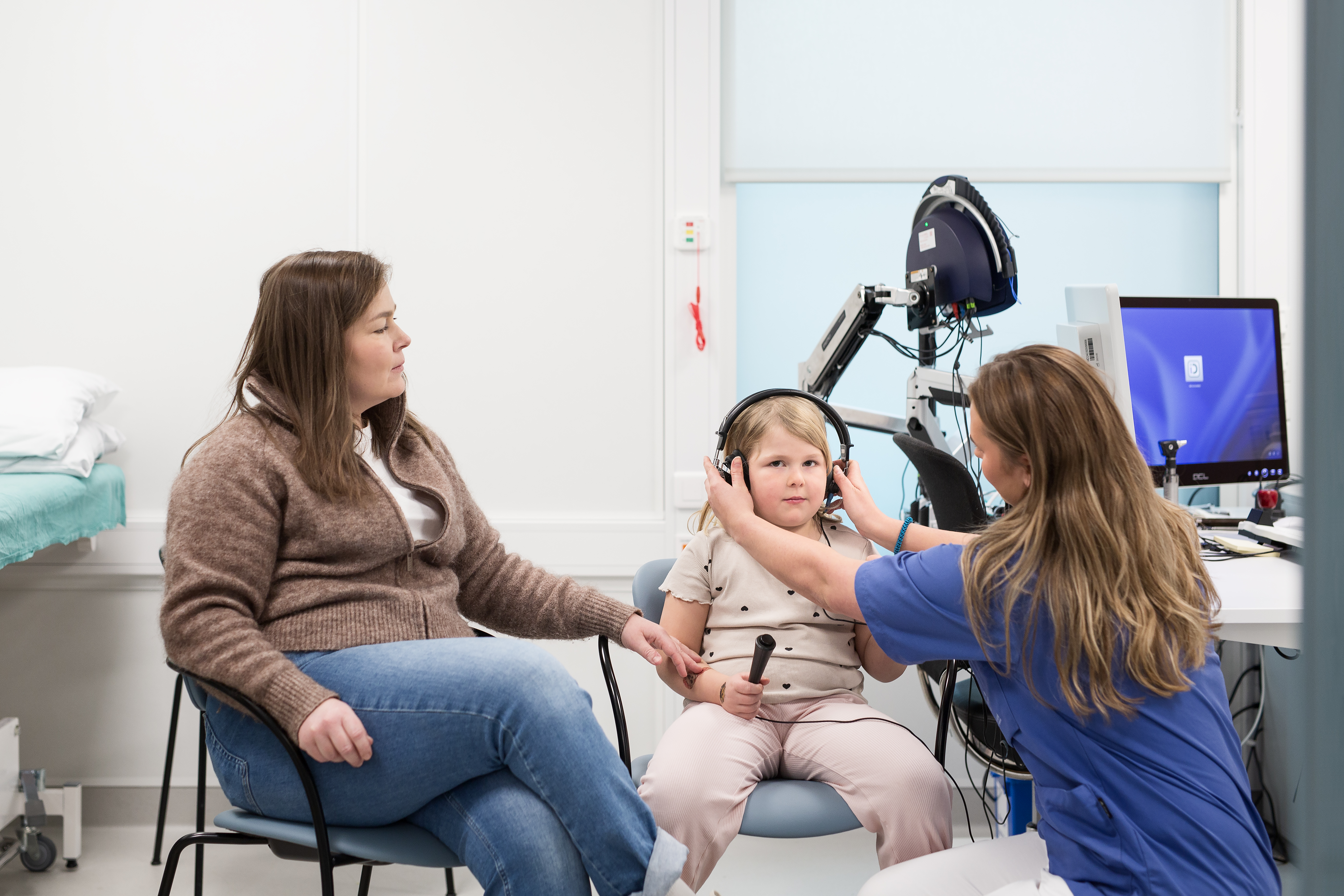 en kvinne i blå uniform som tar på et barn hodetelefoner. En voksen kvinne sitter ved siden av barnet