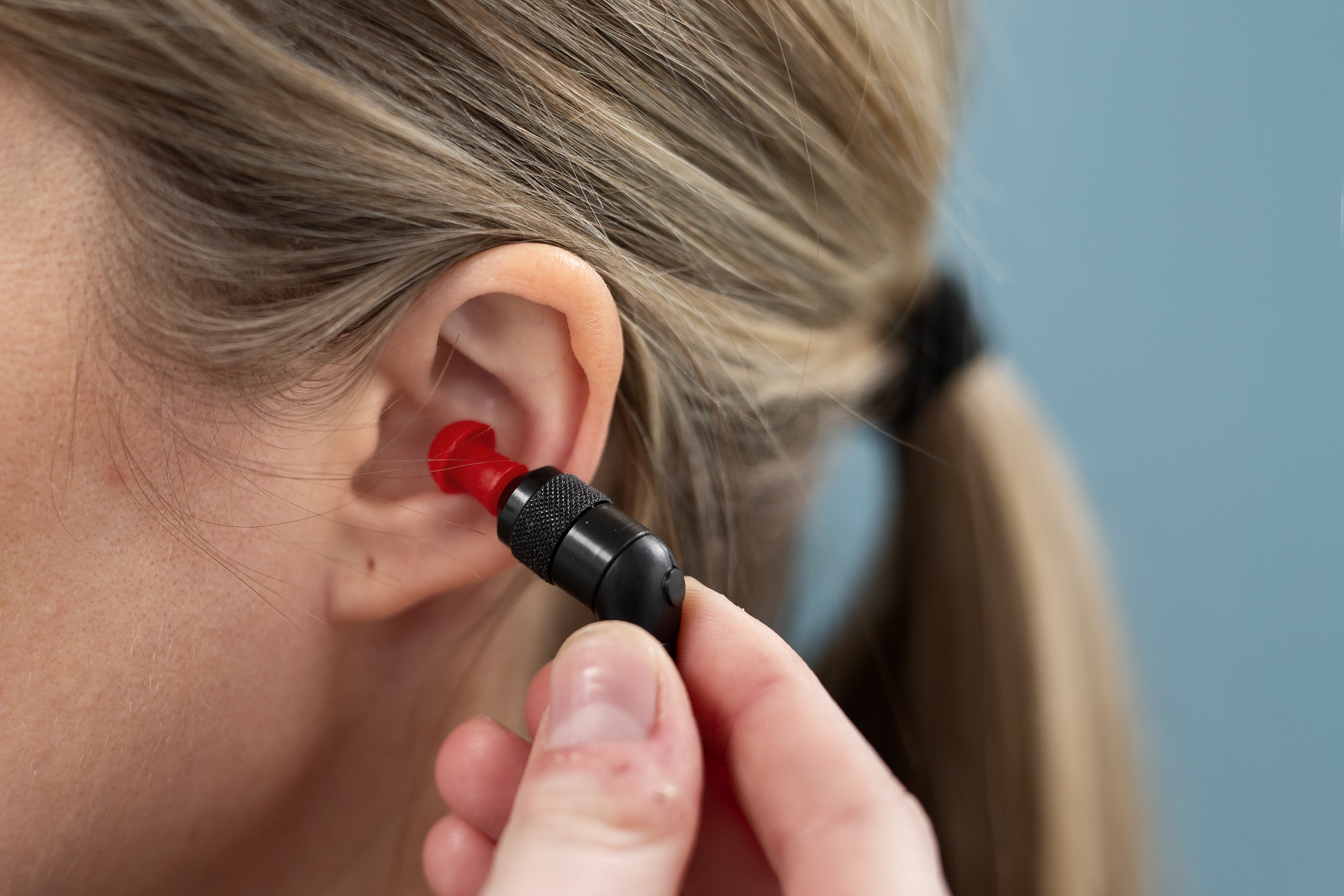 En hånd som plasserer en propp inn i øret til en jente