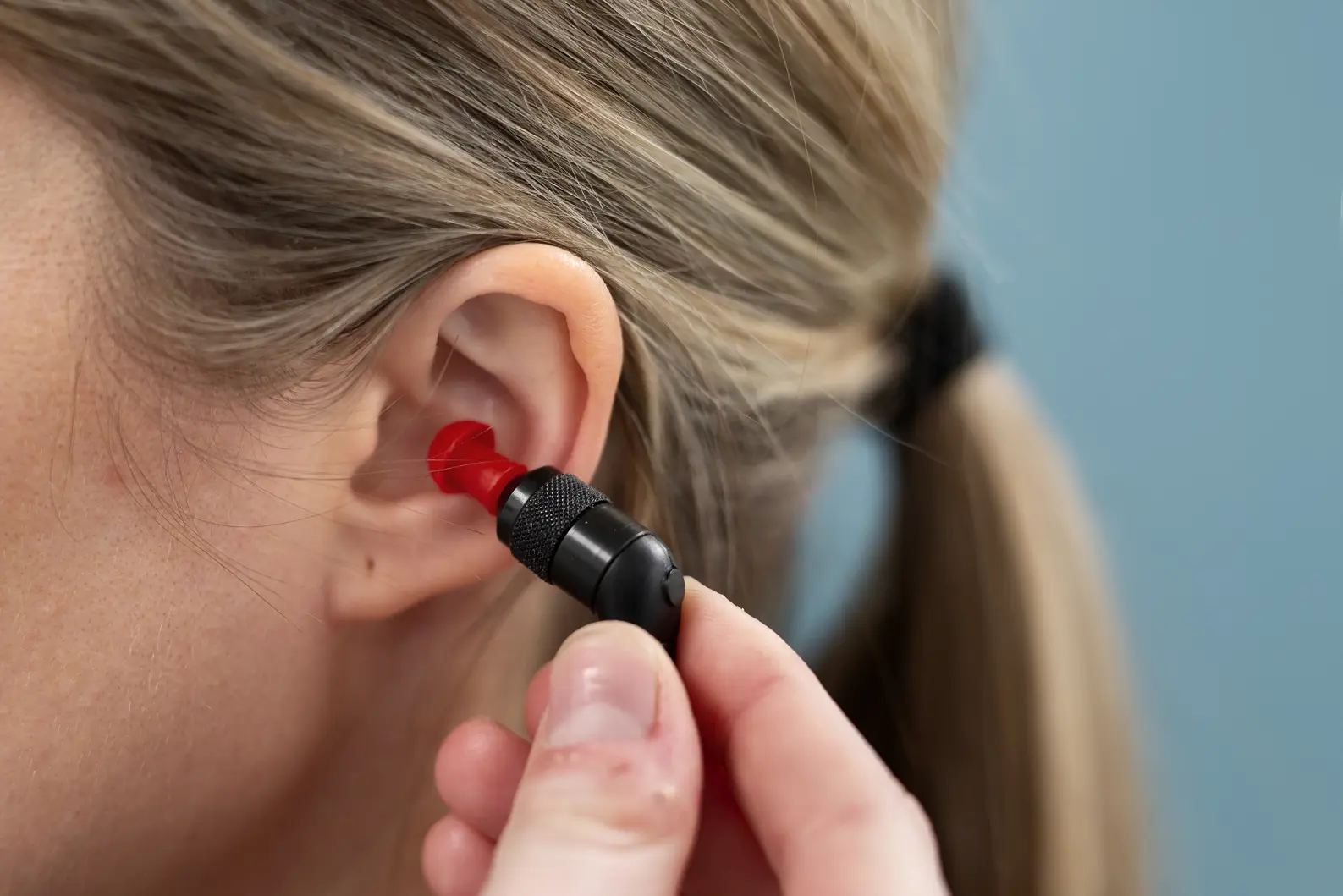 En hånd som plasserer en propp inn i øret til en jente