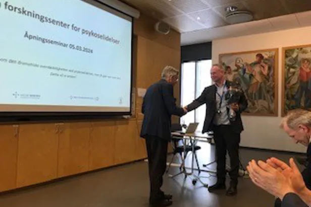 En gruppe menn i dress står foran en projektorskjerm