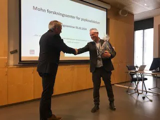 En mann som håndhilser på en annen mann foran en projeksjonsskjerm