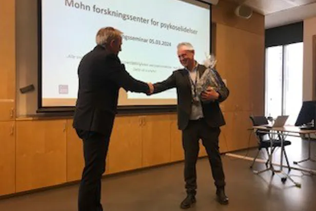 En mann som håndhilser på en annen mann foran en projeksjonsskjerm