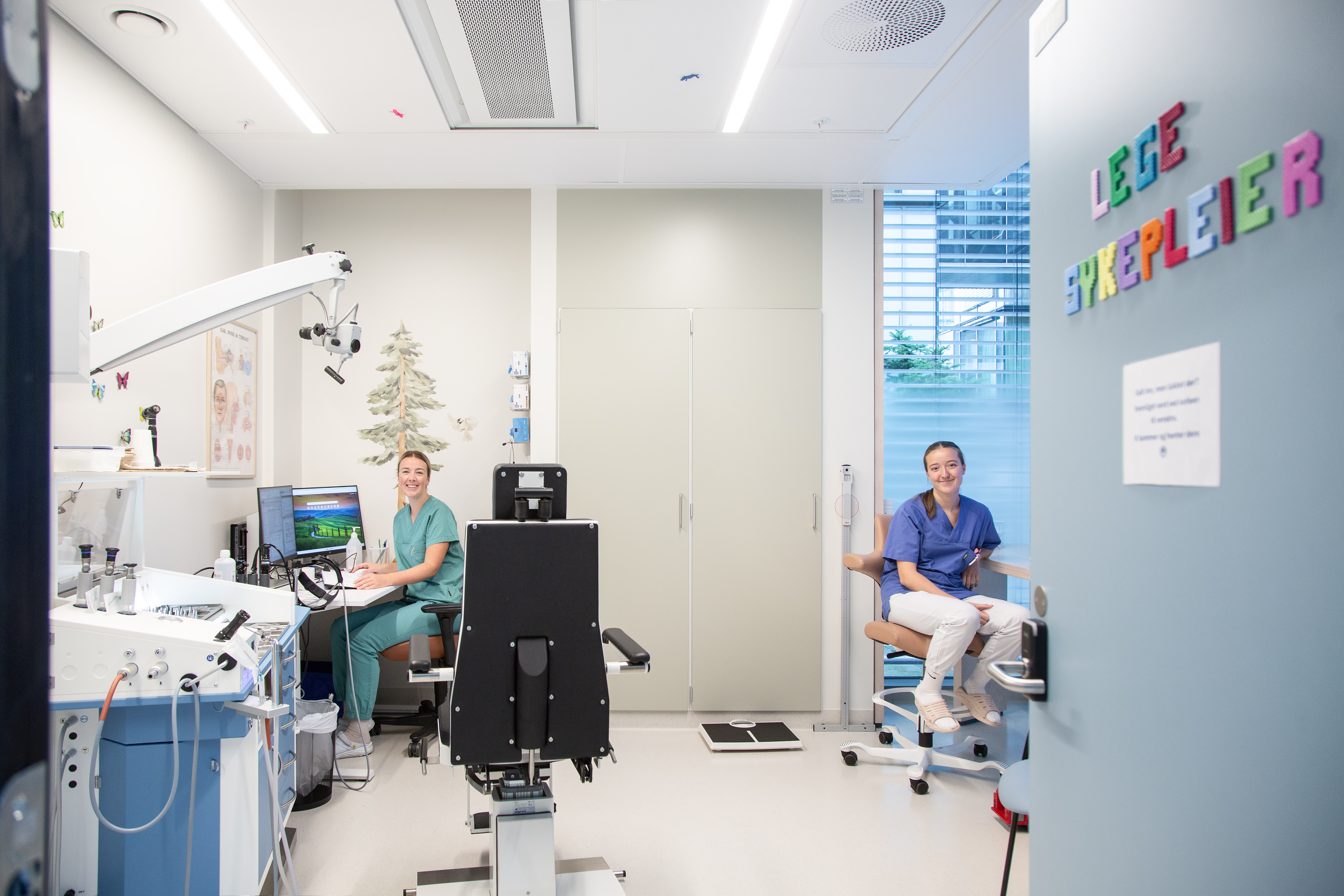 En lege og sykepleier i et rom med undersøkelsesstol, pc og medisinske apparater