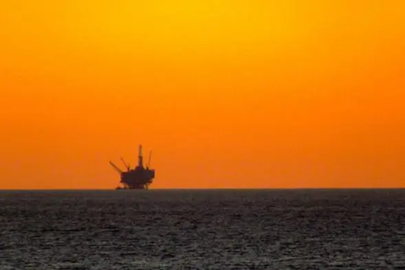 Plattform ute på havet med oransje himmel i bakgrunnen.Foto