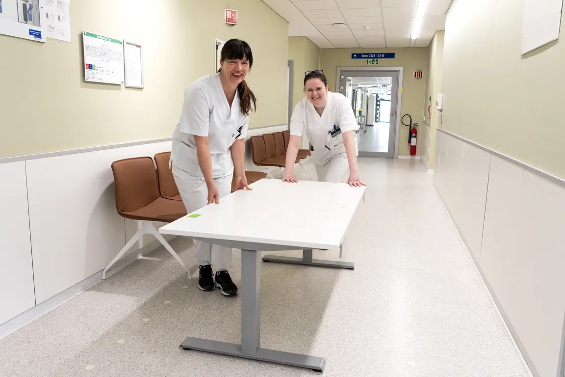 Et par kvinner i hvite laboratoriefrakker som står ved siden av et bord