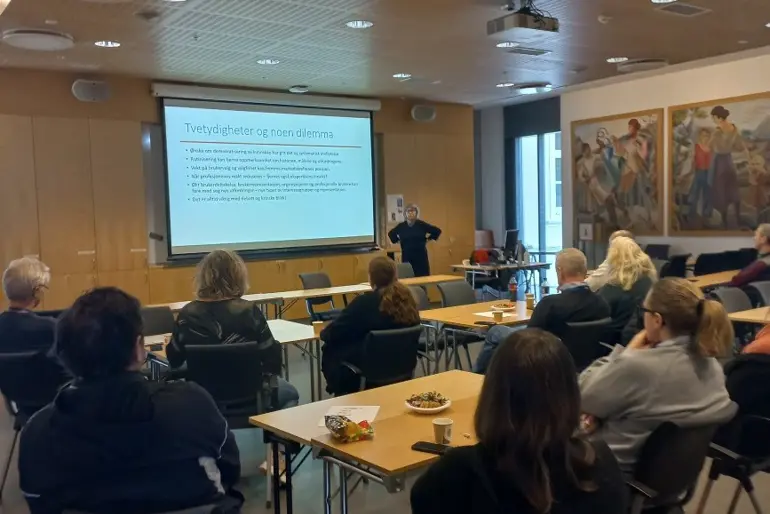En gruppe mennesker som sitter ved bord og ser på en presentasjon