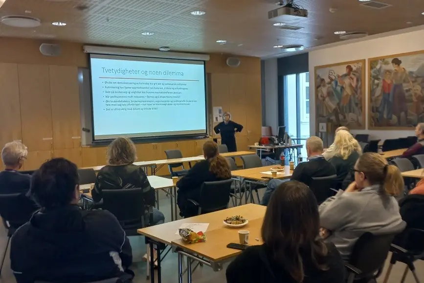 En gruppe mennesker som sitter ved bord og ser på en presentasjon