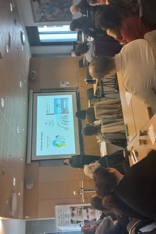 En gruppe mennesker som sitter ved bord og ser på en presentasjon