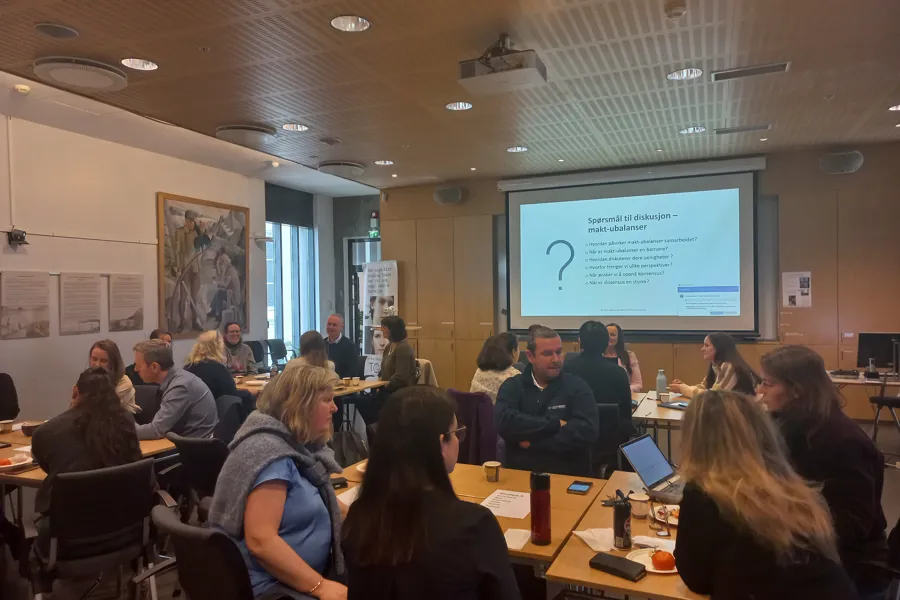 En gruppe mennesker som sitter i et rom og ser på en skjerm