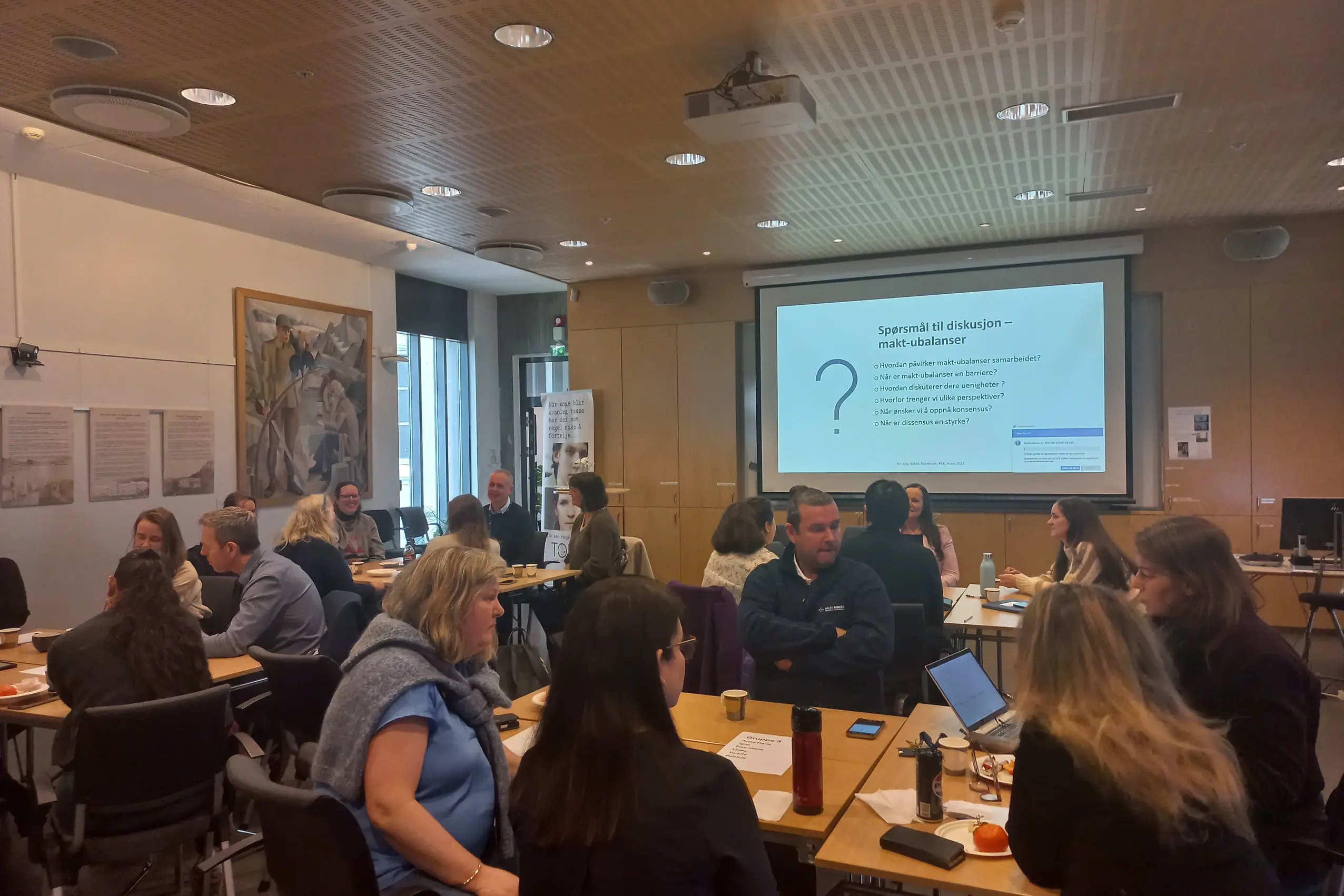 En gruppe mennesker som sitter i et rom og ser på en skjerm