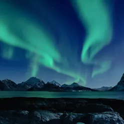 Northern lights in the night over the Lofoten islands in Northern Norway, with snow on the mountain tops.