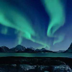 Northern lights in the night over the Lofoten islands in Northern Norway, with snow on the mountain tops.