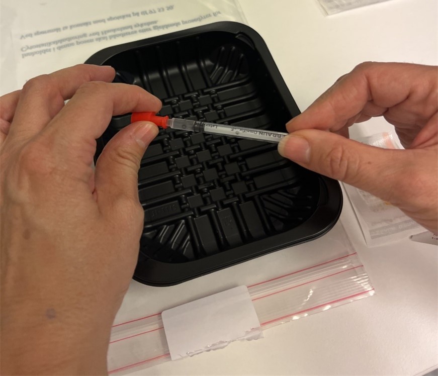 Nærbilde av en som skrur av den røde proppen på sprøyten