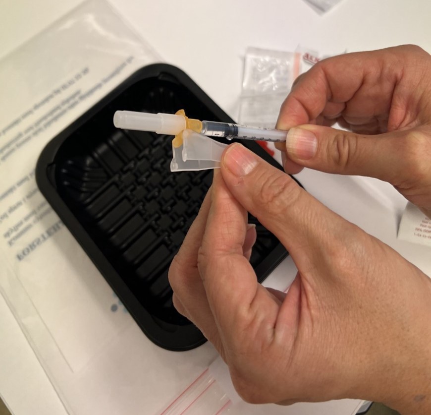 Nærbilde av en person som setter kanylespissen på sprøyten