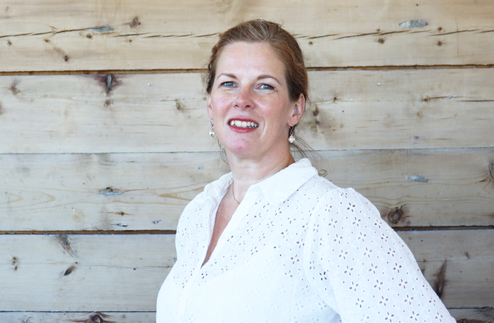 En person som smiler foran en trevegg