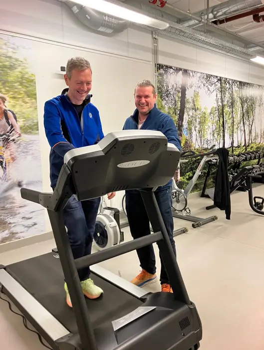 Et par menn som står ved siden av en tredemølle