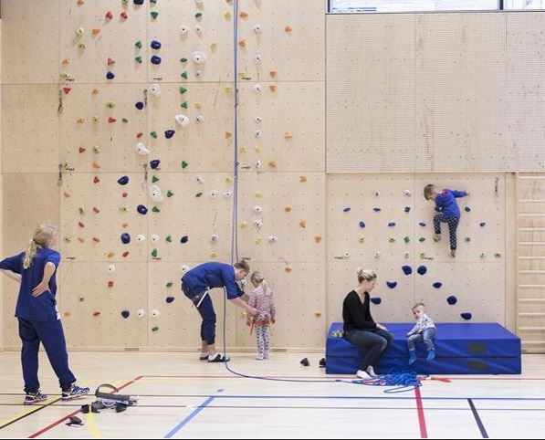 Barn og voksne i en gymsal med klatrevegg