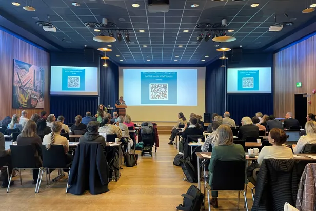 A group of people sitting in a room with a large screen
