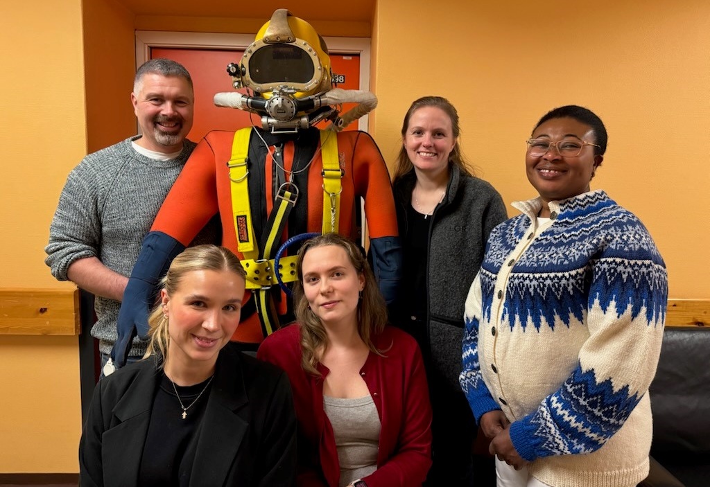 A group of people posing for a photo with a person in a diving garment