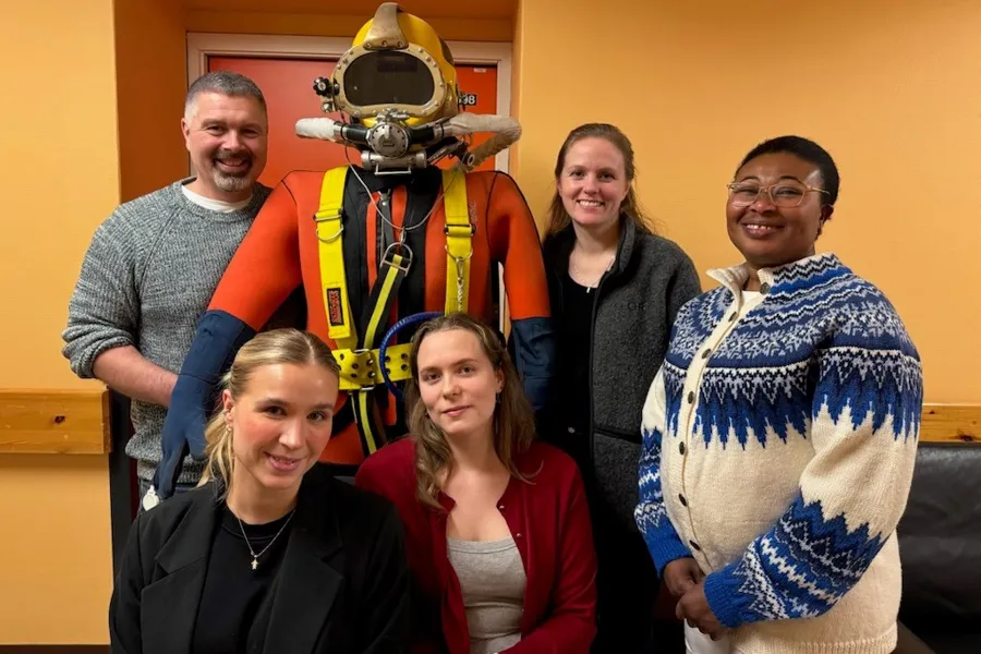 A group of people posing for a photo with a person in a diving garment