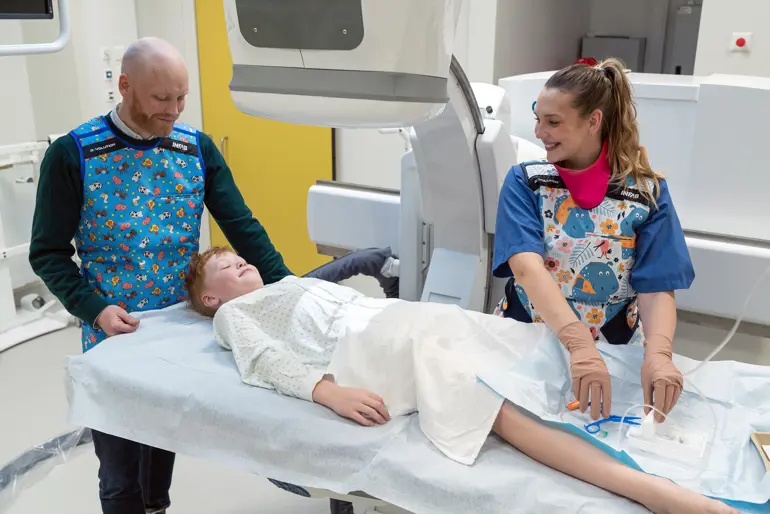 En mann og en radiograf og en gutt som ligger på en benk