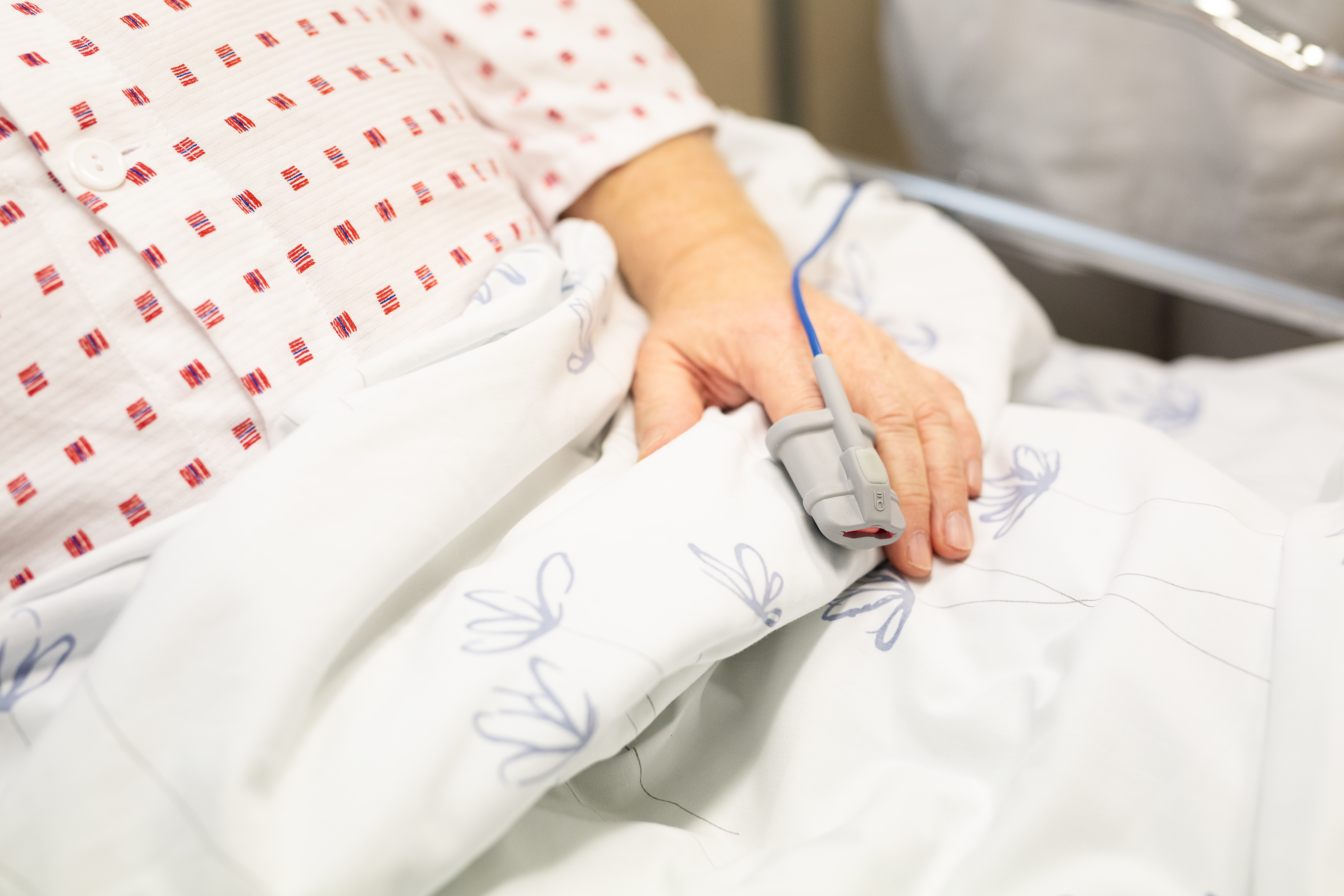 Bilde av hånden til en pasient som ligger i en sykehusseng og får målt metning