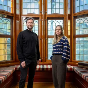 Ein mann og ei kvinne som står foran eit stort blyglasvindauge