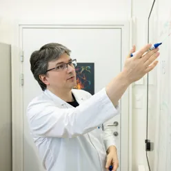 A man in lab coat writing on a whiteboard