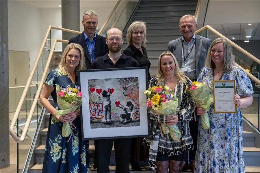 En gruppe mennesker som holder blomster og en plakett