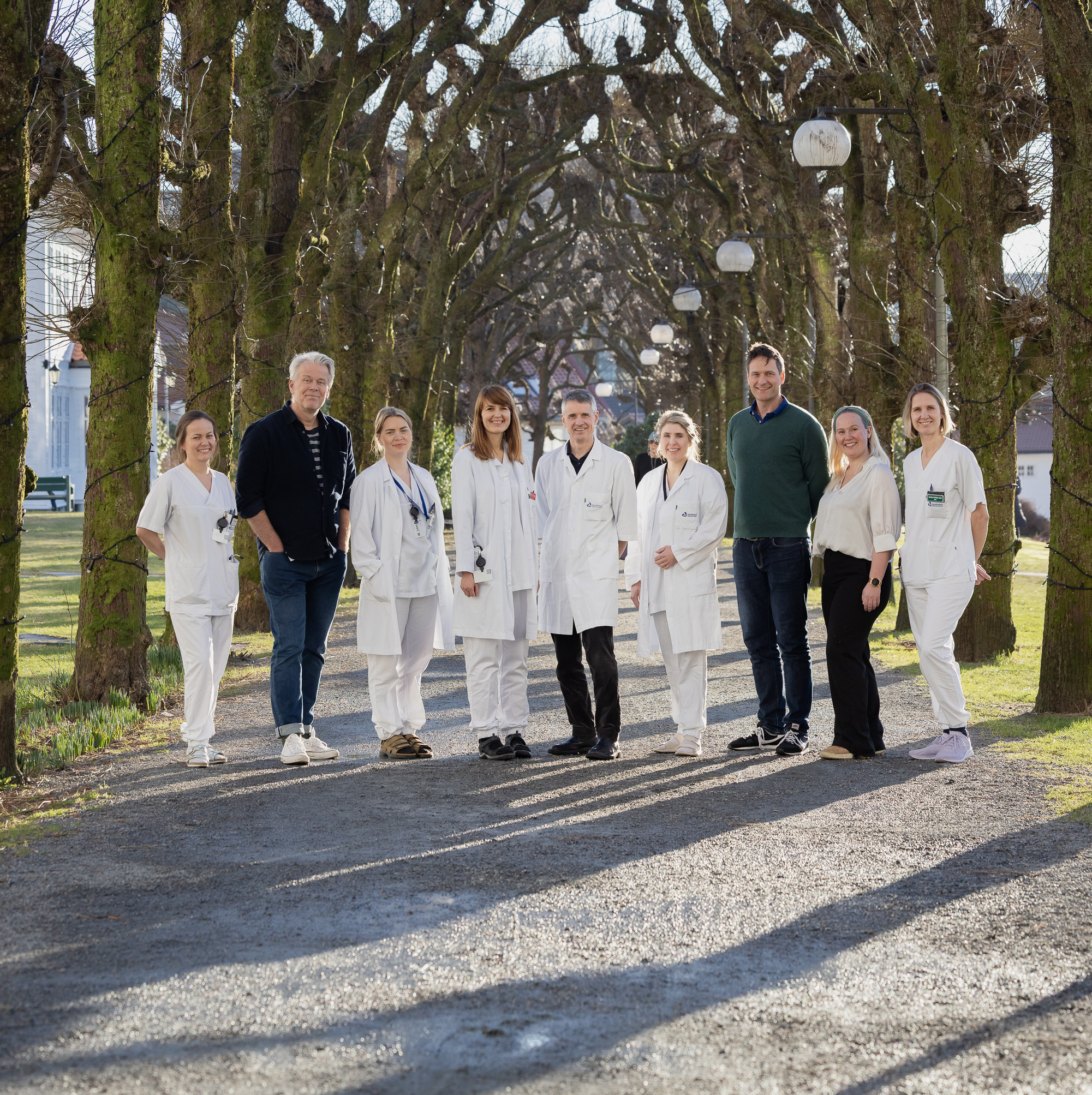 9 personar som står og smiler til kamera, mange med legefrakk.