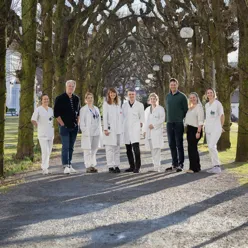 9 people in a group smiling at the camera, several with doctors' coat.