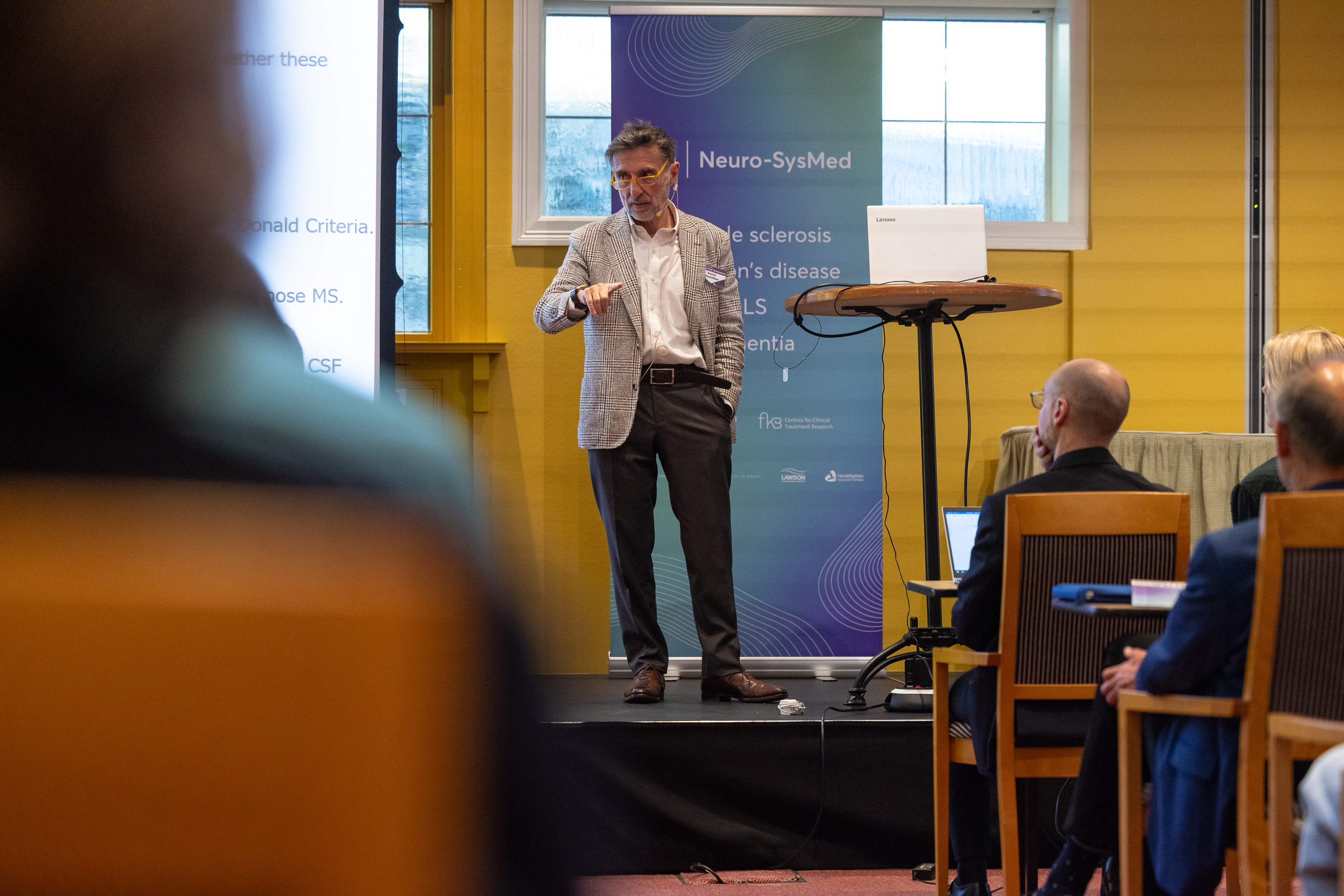 Xavier Montalban står foran et podium med en mikrofon med publikum foran seg